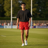 Ruggers Rugby Supply Auckland rugby shorts in red with a black t-shirt, worn by a male athlete on a rugby field.