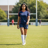 Ruggers Rugby Supply Warrior II navy blue performance jersey with red trim worn by a female athlete on a rugby pitch